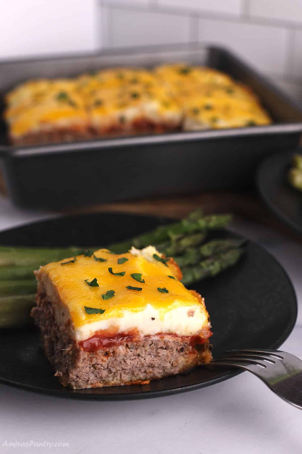 A piece of meatloaf casserole on a black plate with a fork next to it.