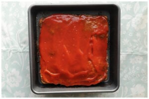 Meatloaf in the pan with ketchup spread over the top.