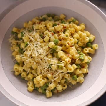 A zoom in image of a grey plate with pasta and peas.