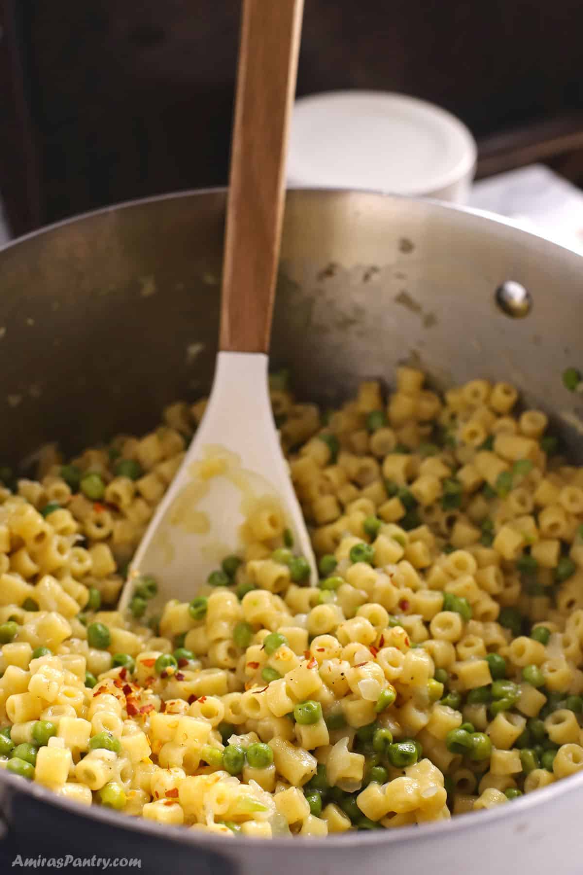 Pasta with peas in a stainless steel pot garnished with pepper flakes.