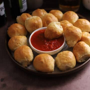 Pizza balls on a serving platter with one dipped into a bowl of sauce.