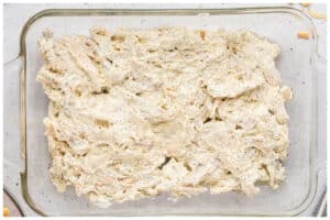 Chicken poppyseed mixture spread at the bottom of a glass casserole dish.