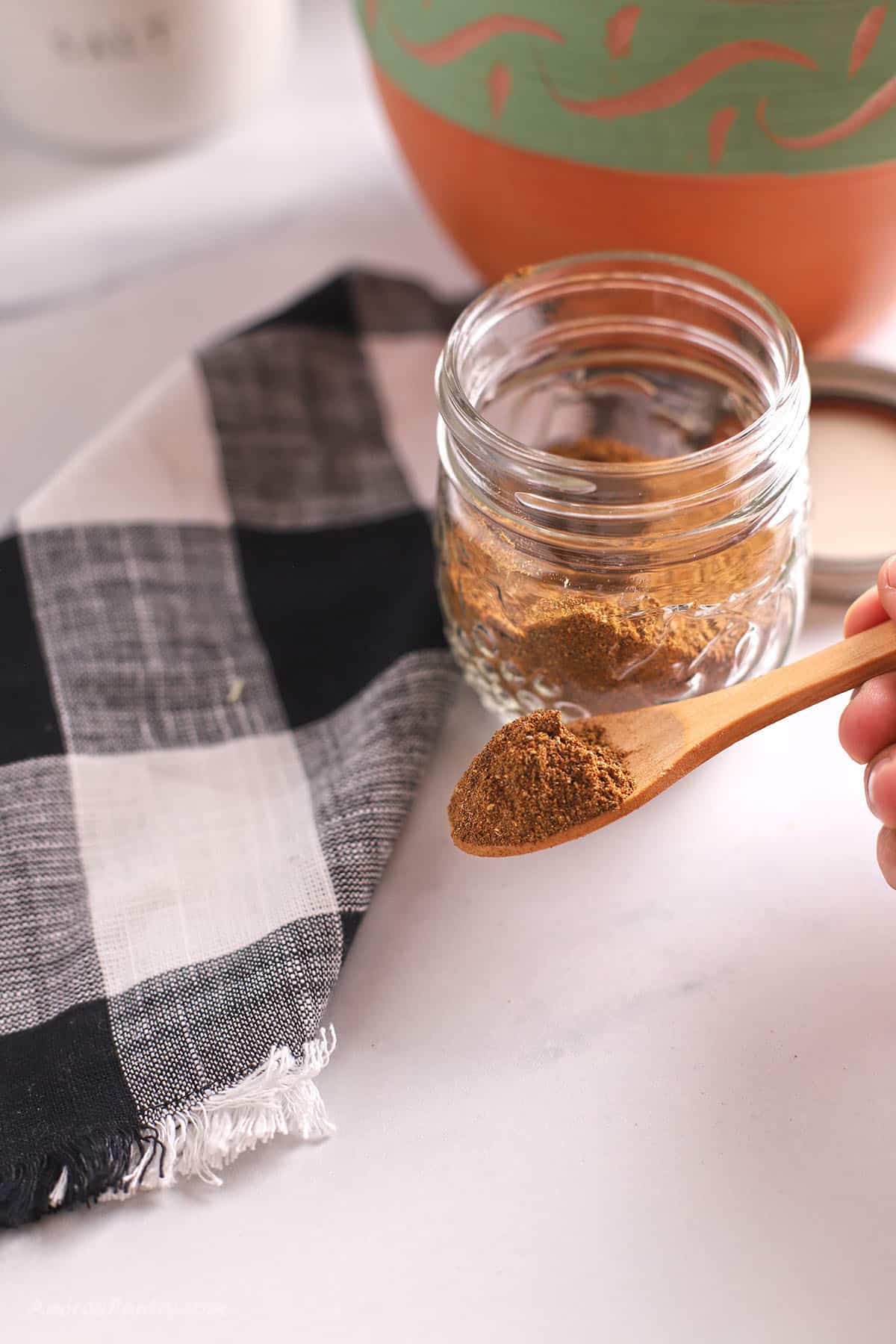 Scooping some shawarma seasoning with a wooden spoon from a glass spice jar.