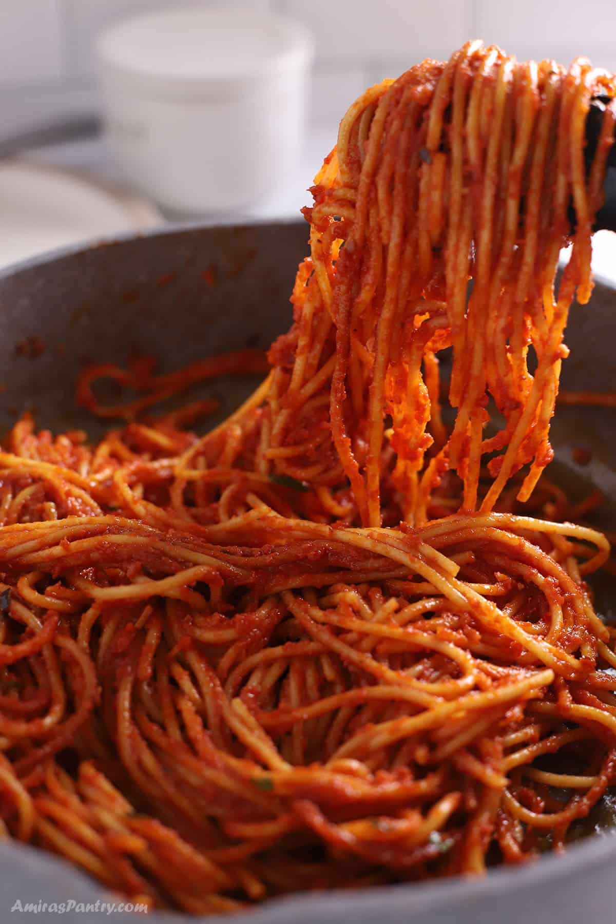 Kitchen tongs with some spaghetti all'assassina over a large skillet.