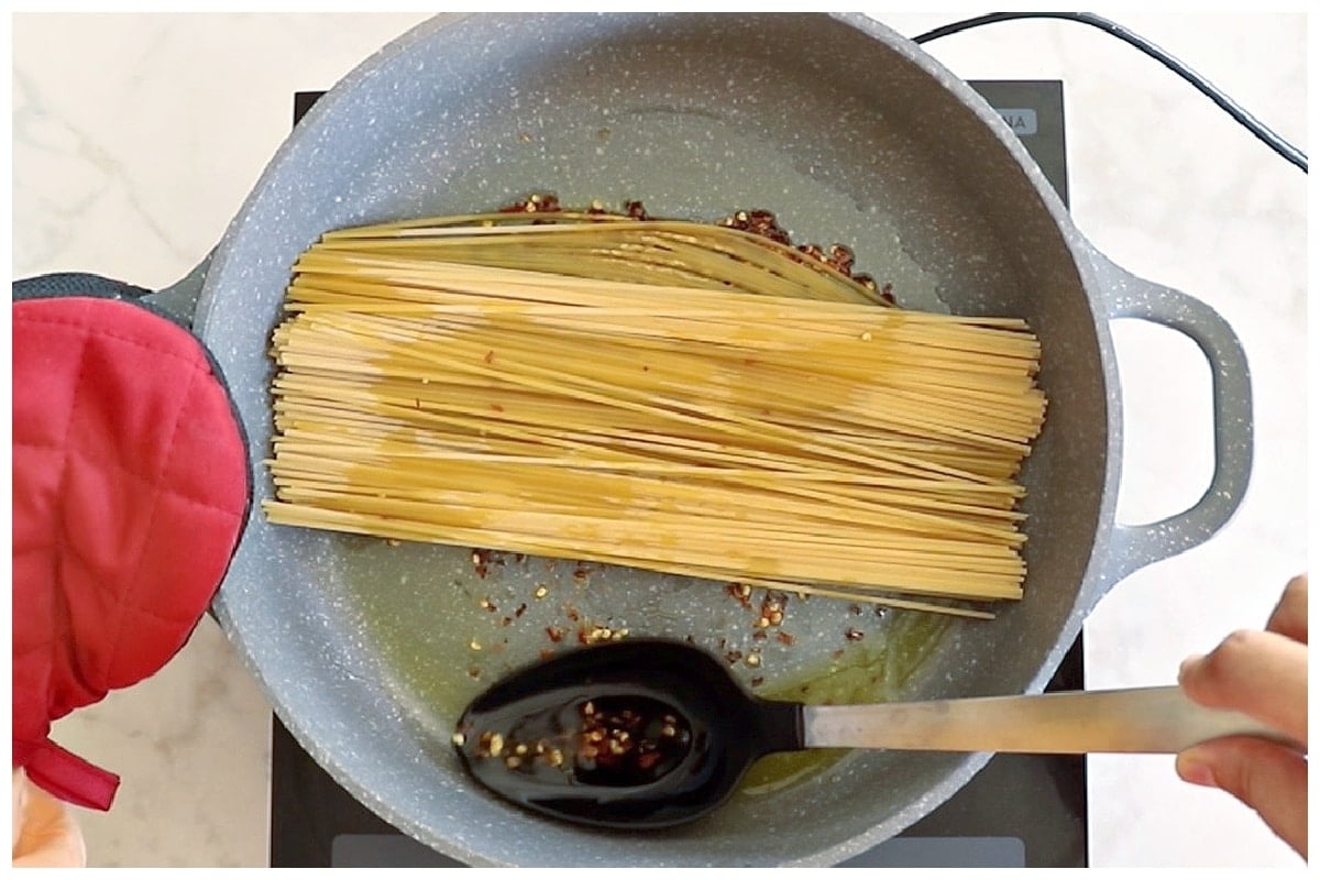 Tilting the pan and scooping chili oil over pasta.