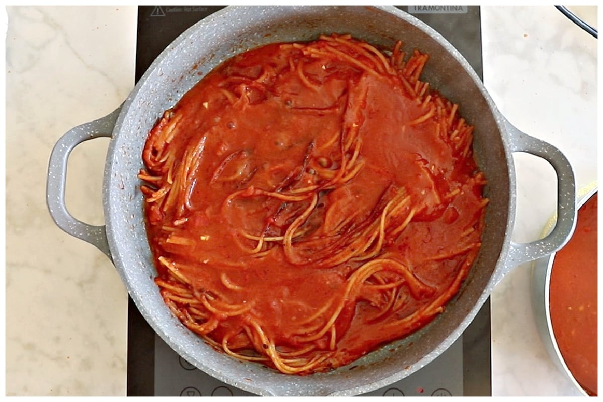 Pouring more tomato sauce over the pasta.