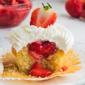 A cupcake on a white surface cut in the middle to show strawberry filling.