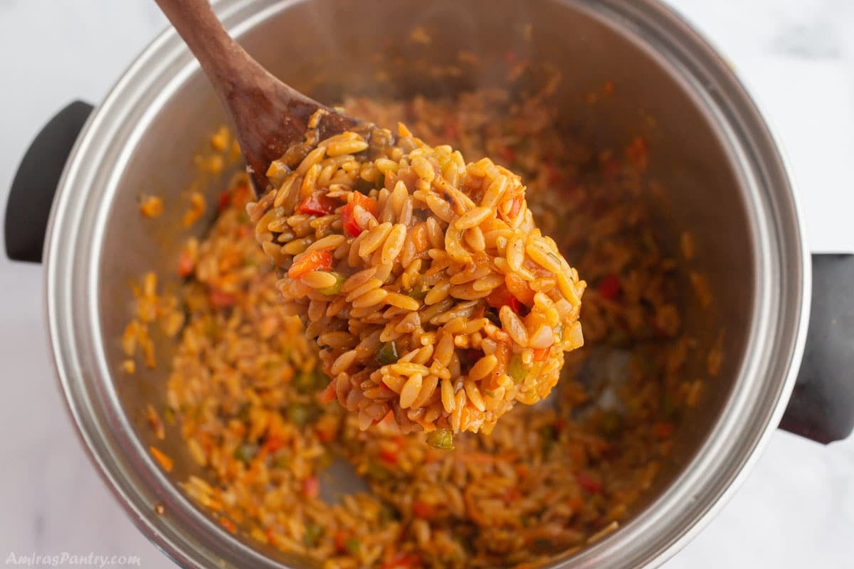 A wooden spoon scooping some vegetarian orzo from the pot.
