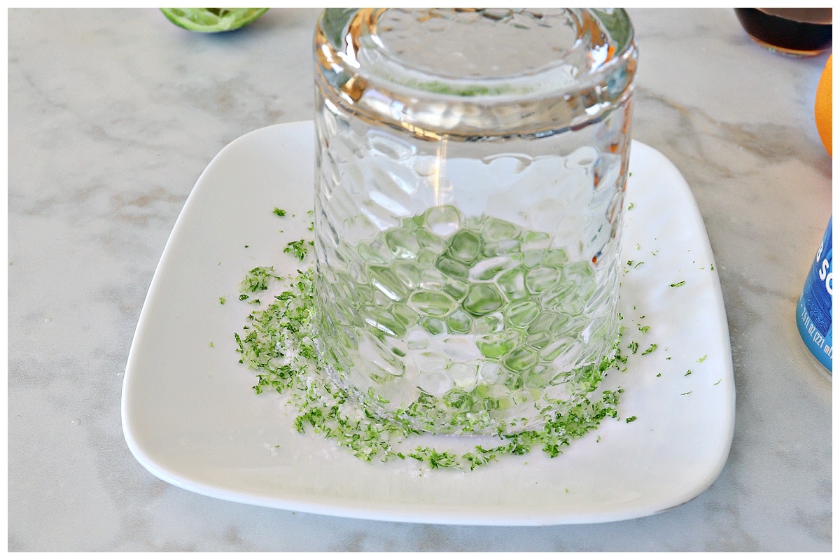 A cup inverted upside down on a plate of salt and lime zest.