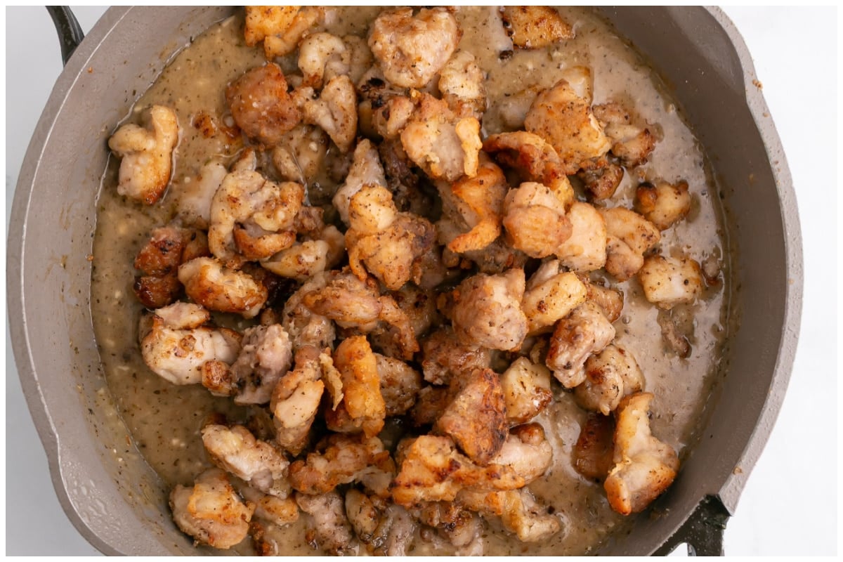 A large skillet with chicken thigh pieces in garlic butter sauce.