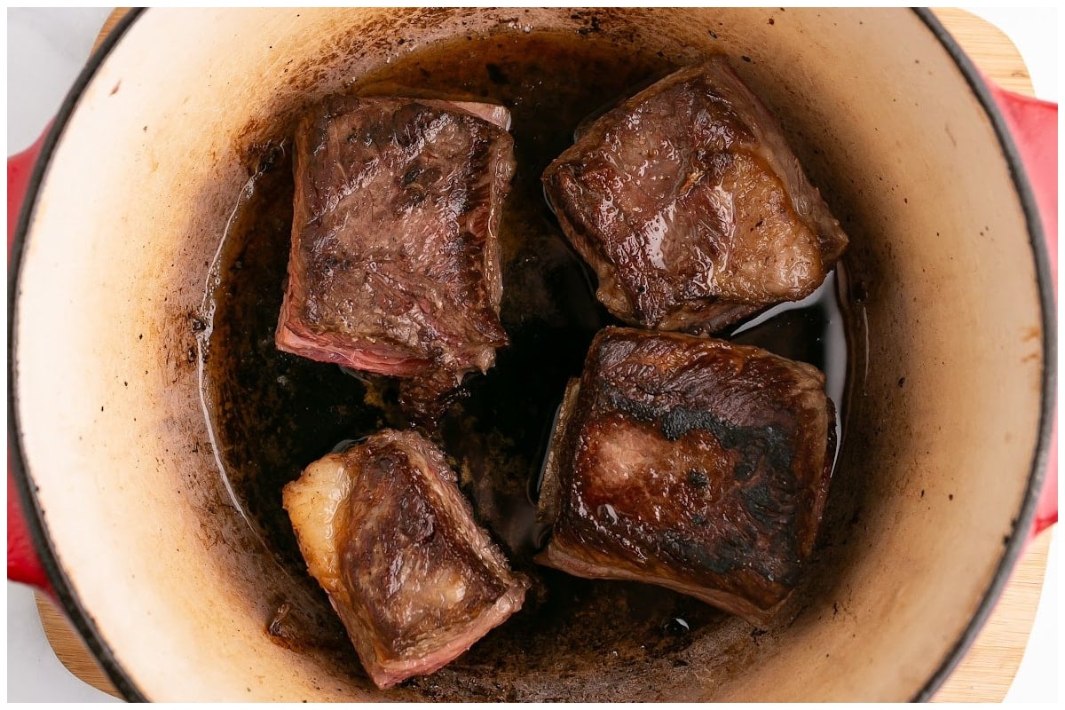 A large dutch oven with seared short ribs.