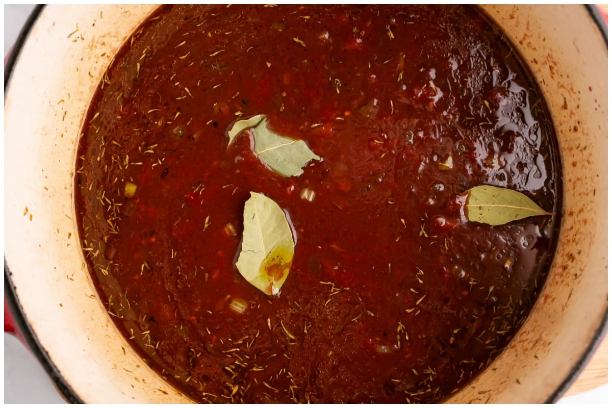 A dutch oven with ragu sauce and spices.