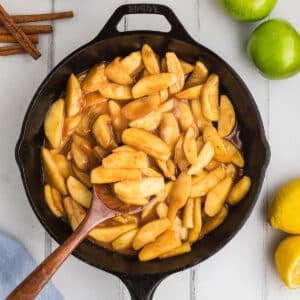 An overhead image of a black skillet with a wooden spoon scooping some fried apples.