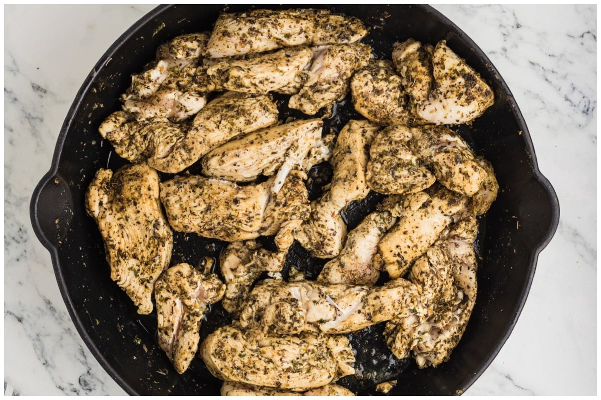 Seasoned chicken strips seared in a large pan.