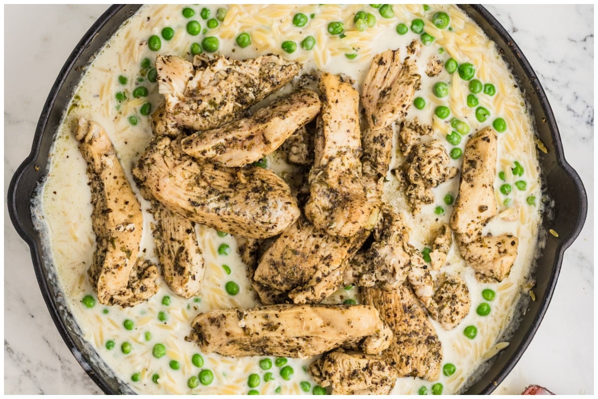 A pot with cooked chicken and orzo with peas.