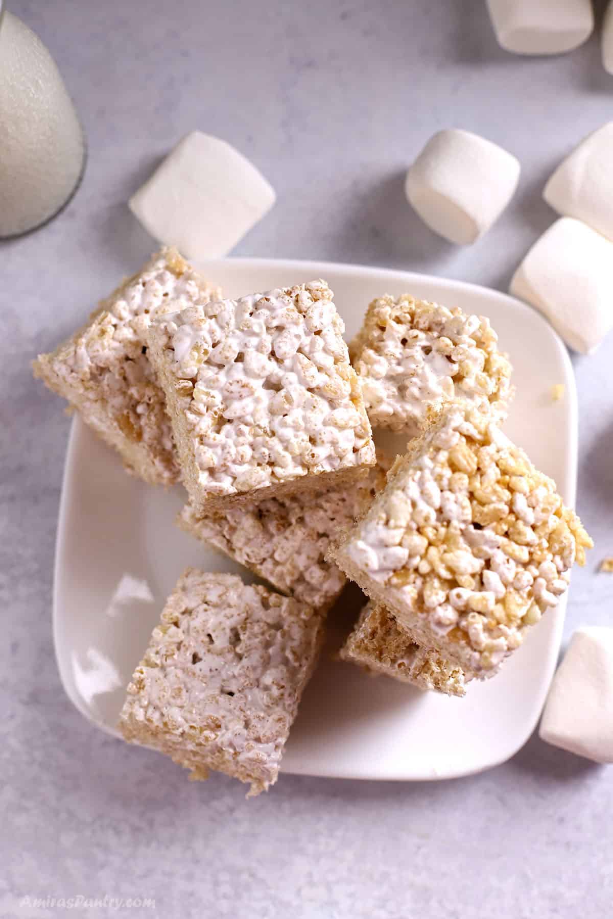 Rice Krsipie squares on a white plate with marshmallows in the back.