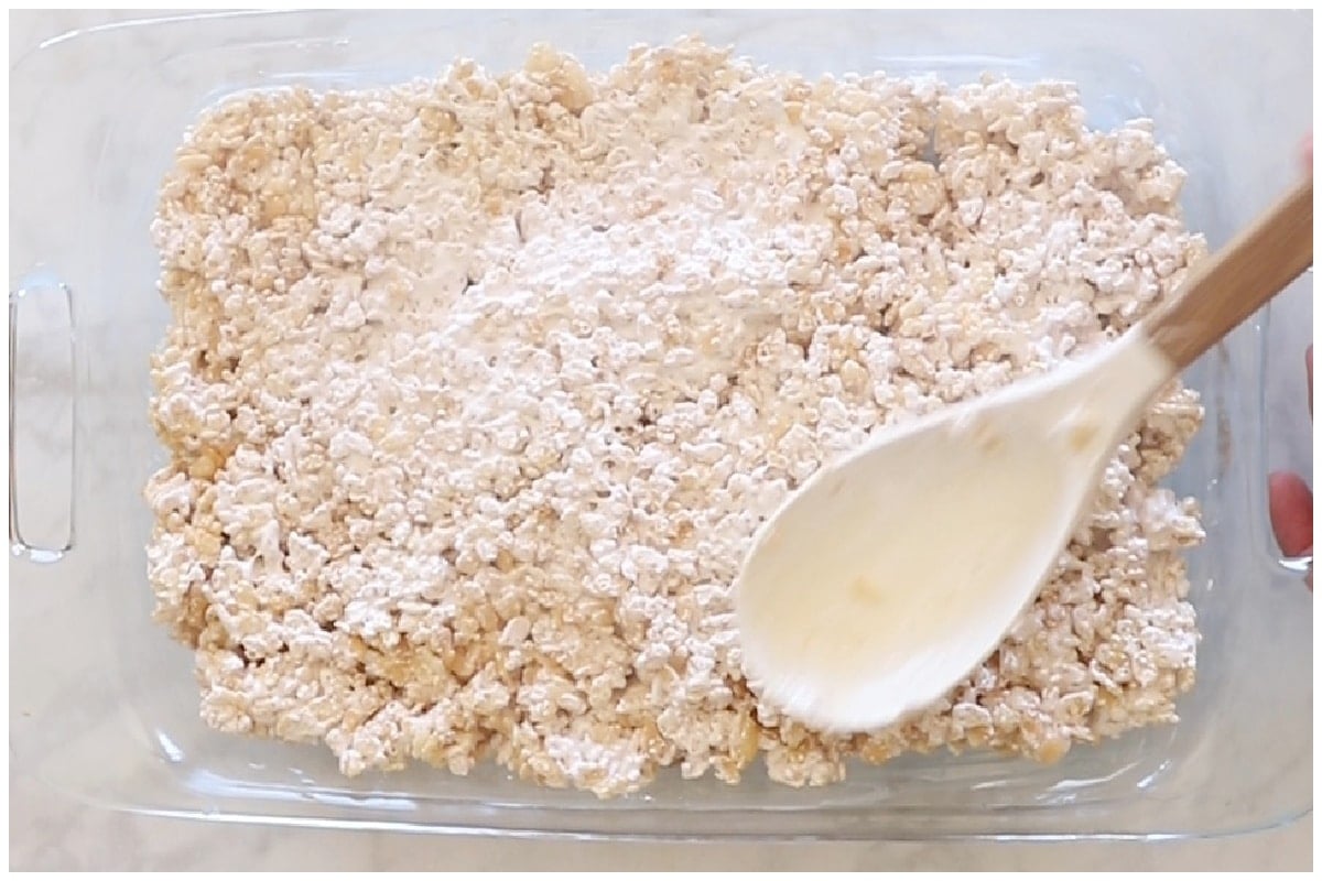 Rice krispie treats on a glass casserole with a spoon pressing on it.