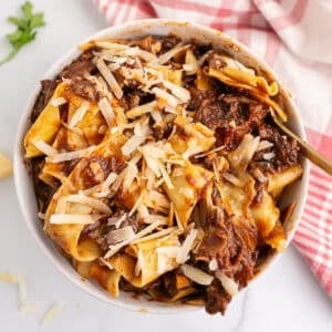 An overhead image of a white bowl with beef ragu garnished with parmesan cheese.