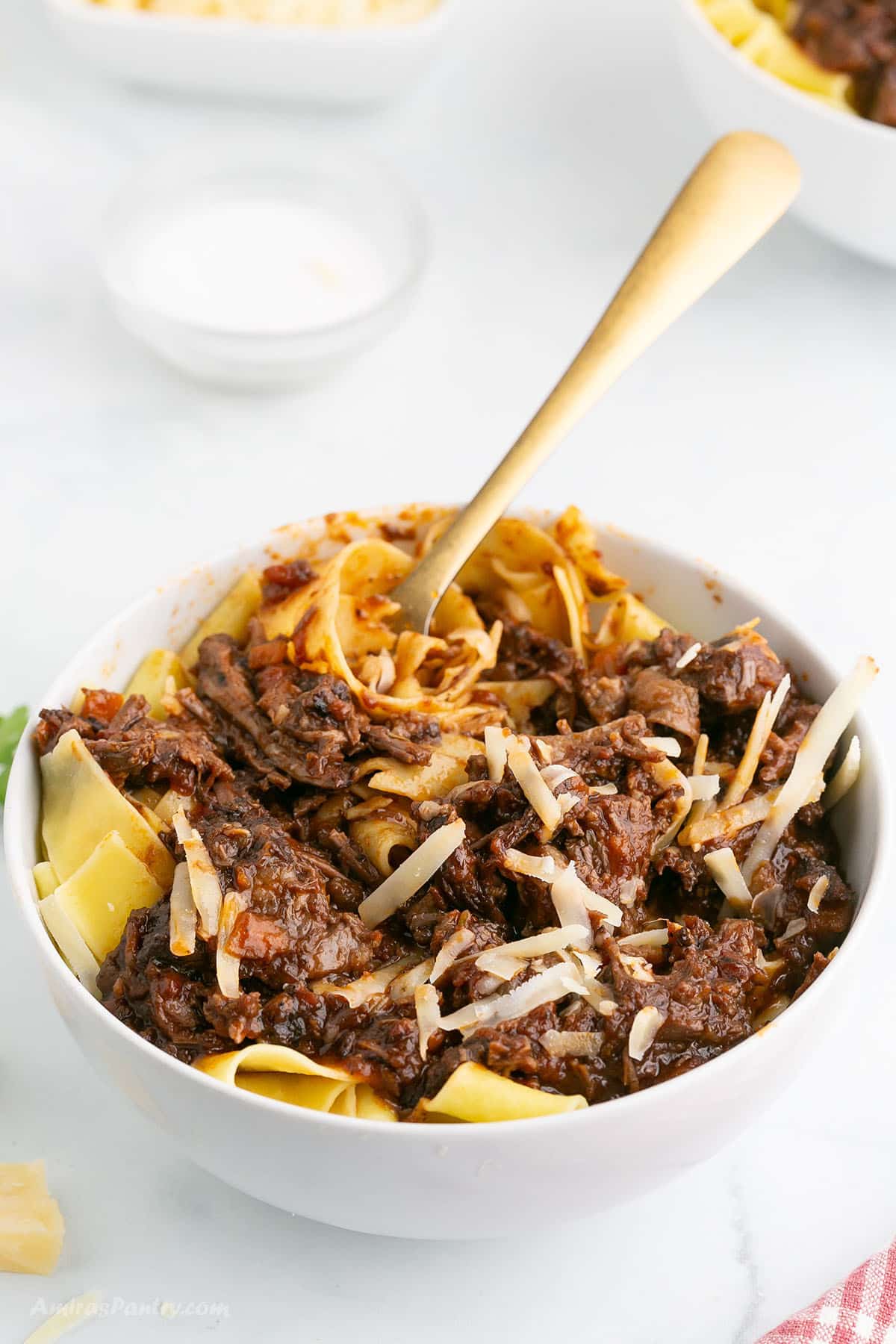 A fork twirled with some ragu pasta in a white bowl.