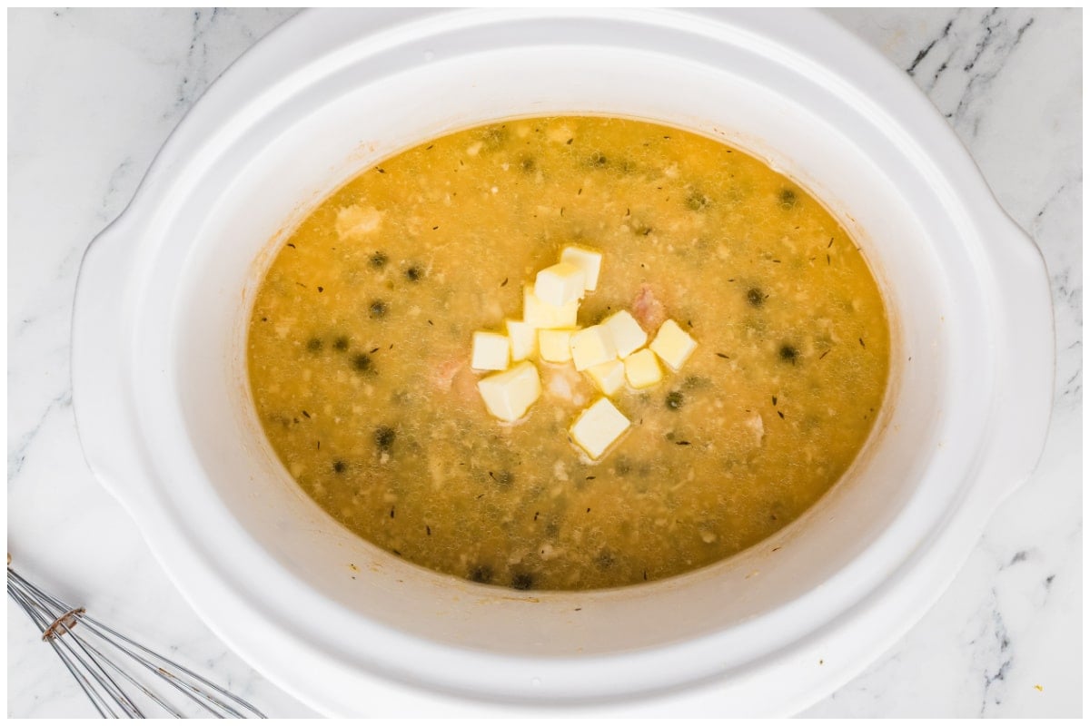 A slow cooker with chicken piccata topped with cubed butter.