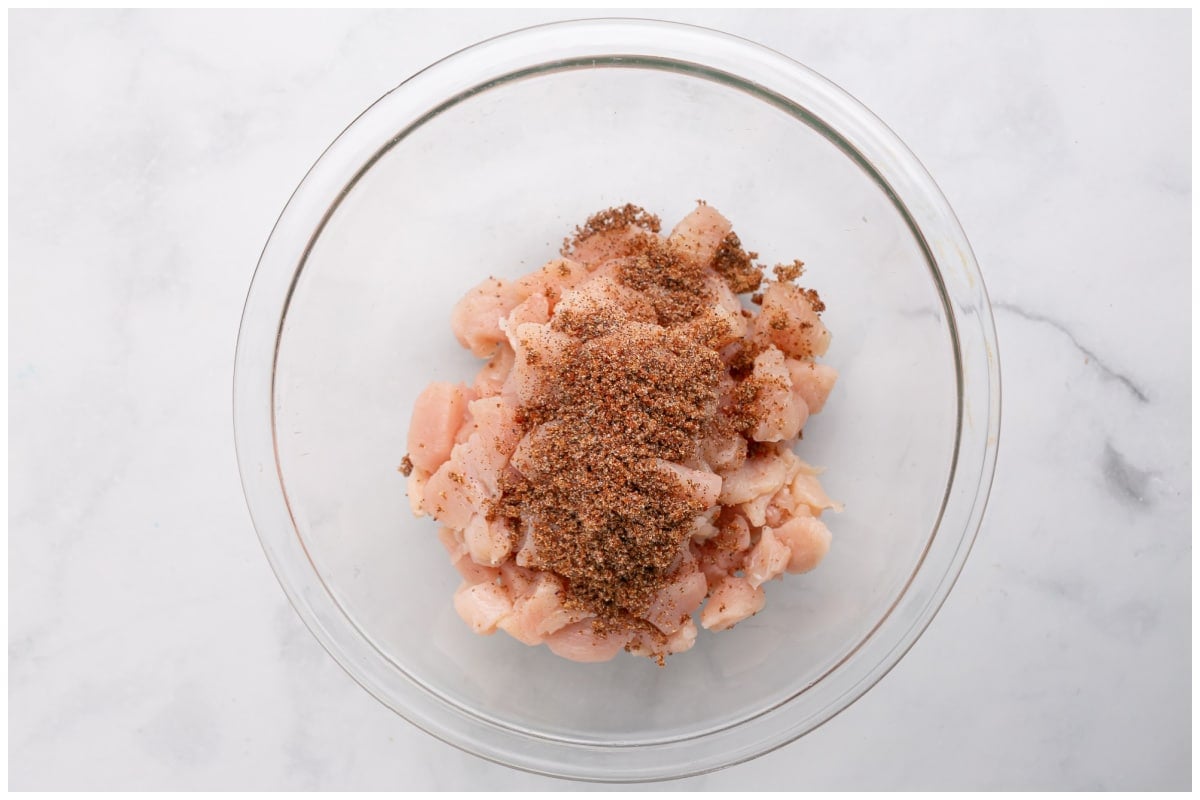 Spices tossed with cubed chicken in a glass bowl.