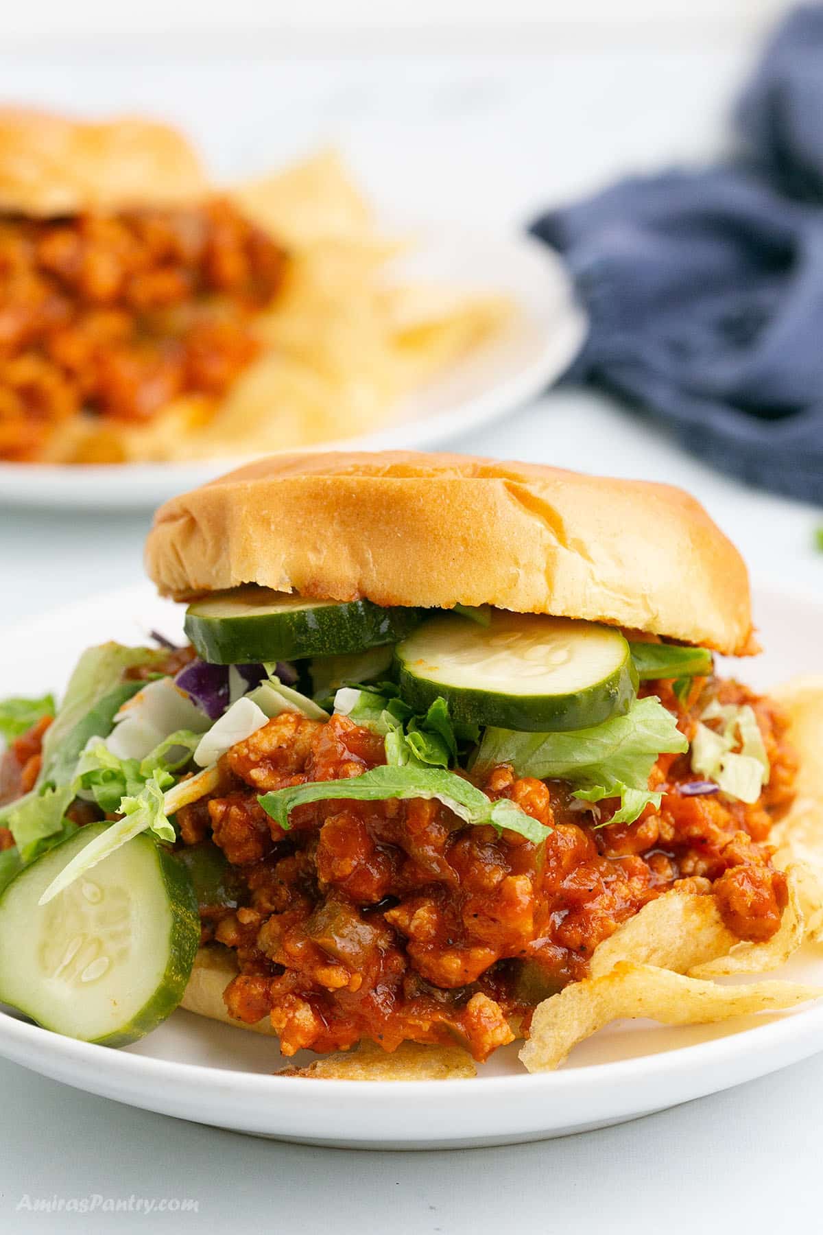 A sloppy joes sandwich with cucumber on a white plate.