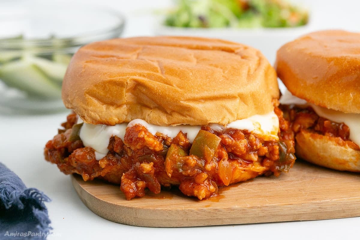 Sloppy Joes Sandwiches with melty cheese on a wooden cutting board.