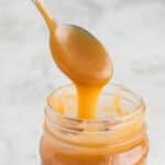 A spoon scooping caramel sauce out of a jar.