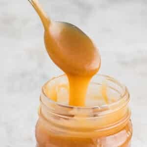 A spoon scooping caramel sauce out of a jar.