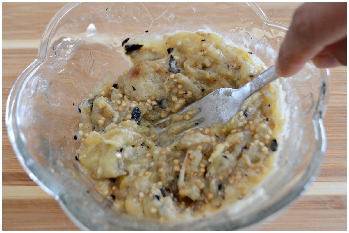 Mashing eggplants in a glass bowl with a fork.