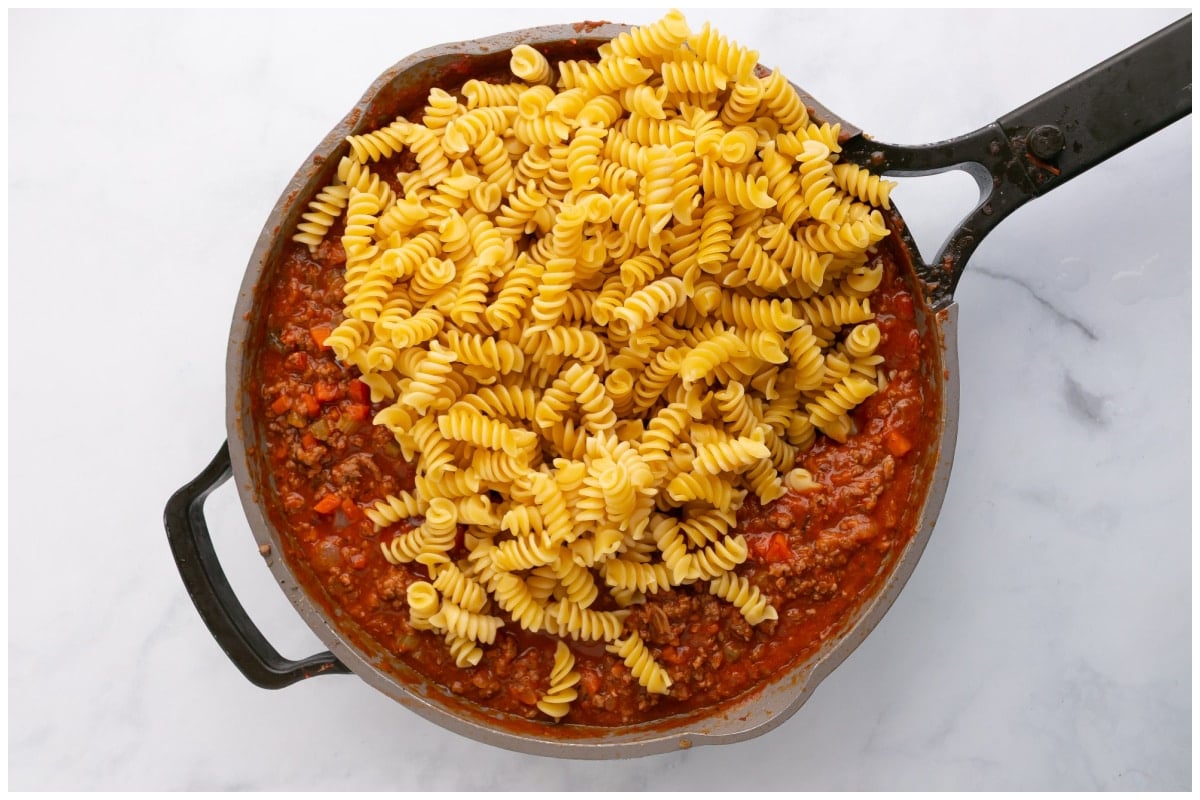 Adding cooked pasta to the meat sauce.