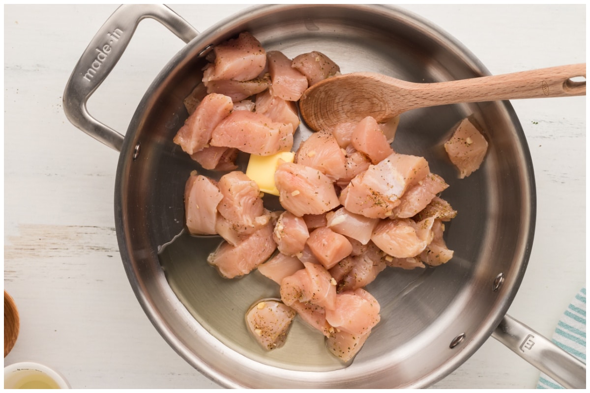 A large skillet with chicken cubes and butter.