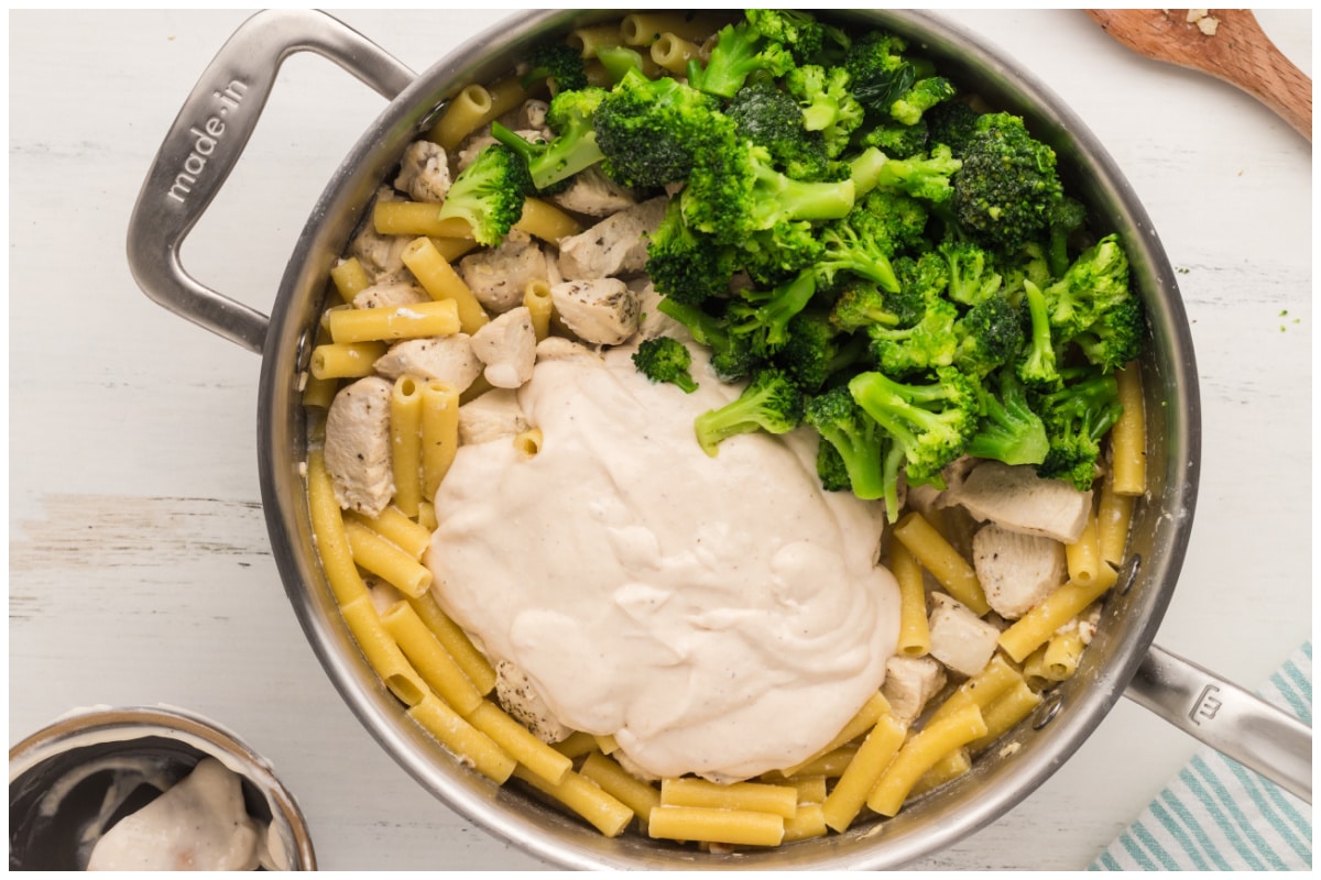 Pouring alfredo sauce and adding broccoli to the pan.