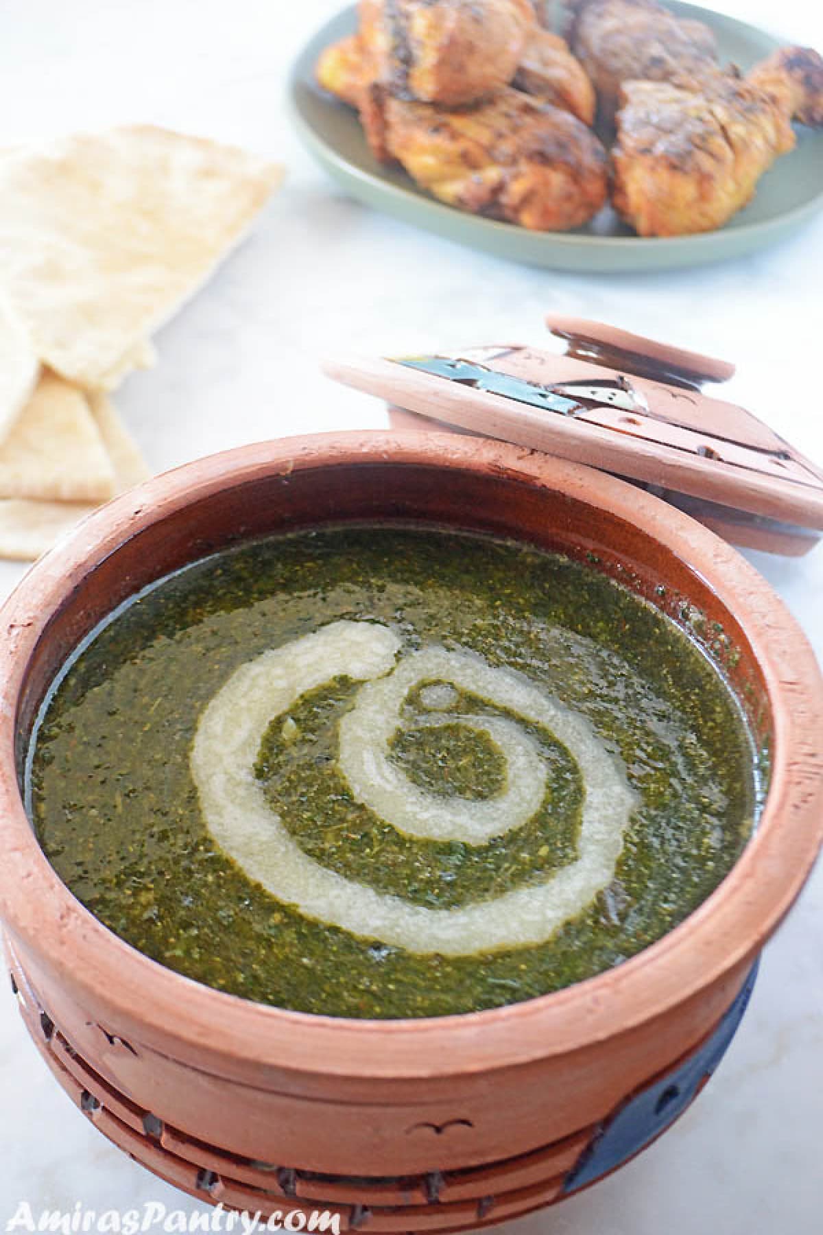 Mulukhia served in a clay pot with pita bread and chicken on the back. The tope is swirled with butter.