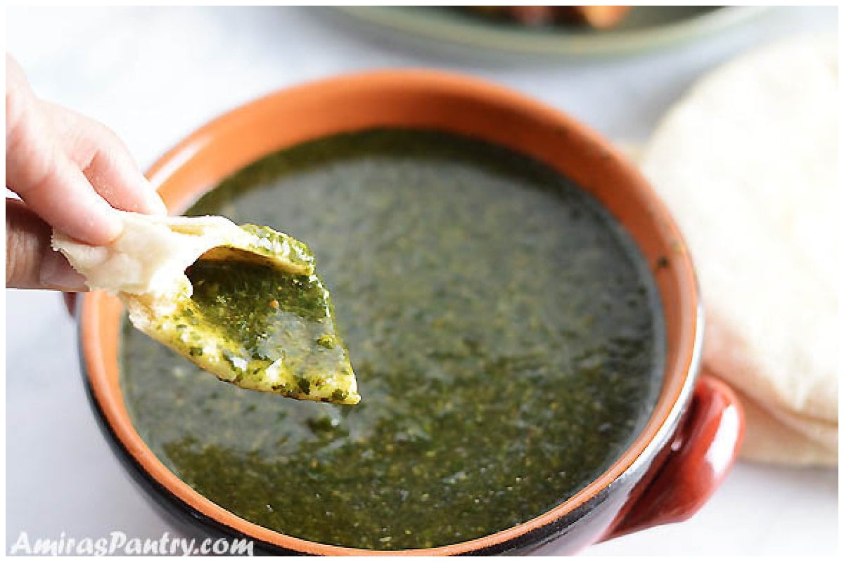 A hand scooping some molokhia soup with a piece of pita bread.