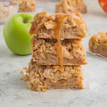 Caramel apple pie bars on a white surface with green apples on the back.