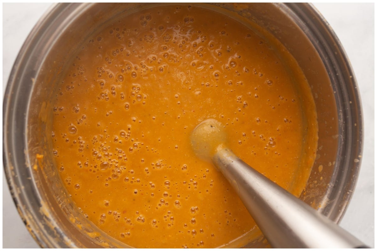 An immersion blender blending soup in a pot. 