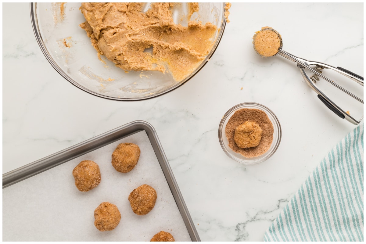 A cookie sheet with cookie dough balls and a cookie scoop on the side.