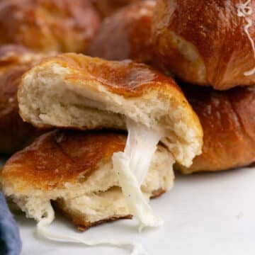 Two halves of a ball of pretzel stacked with the cheese oozing out of the top one.