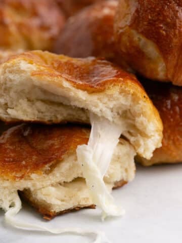 Two halves of a ball of pretzel stacked with the cheese oozing out of the top one.