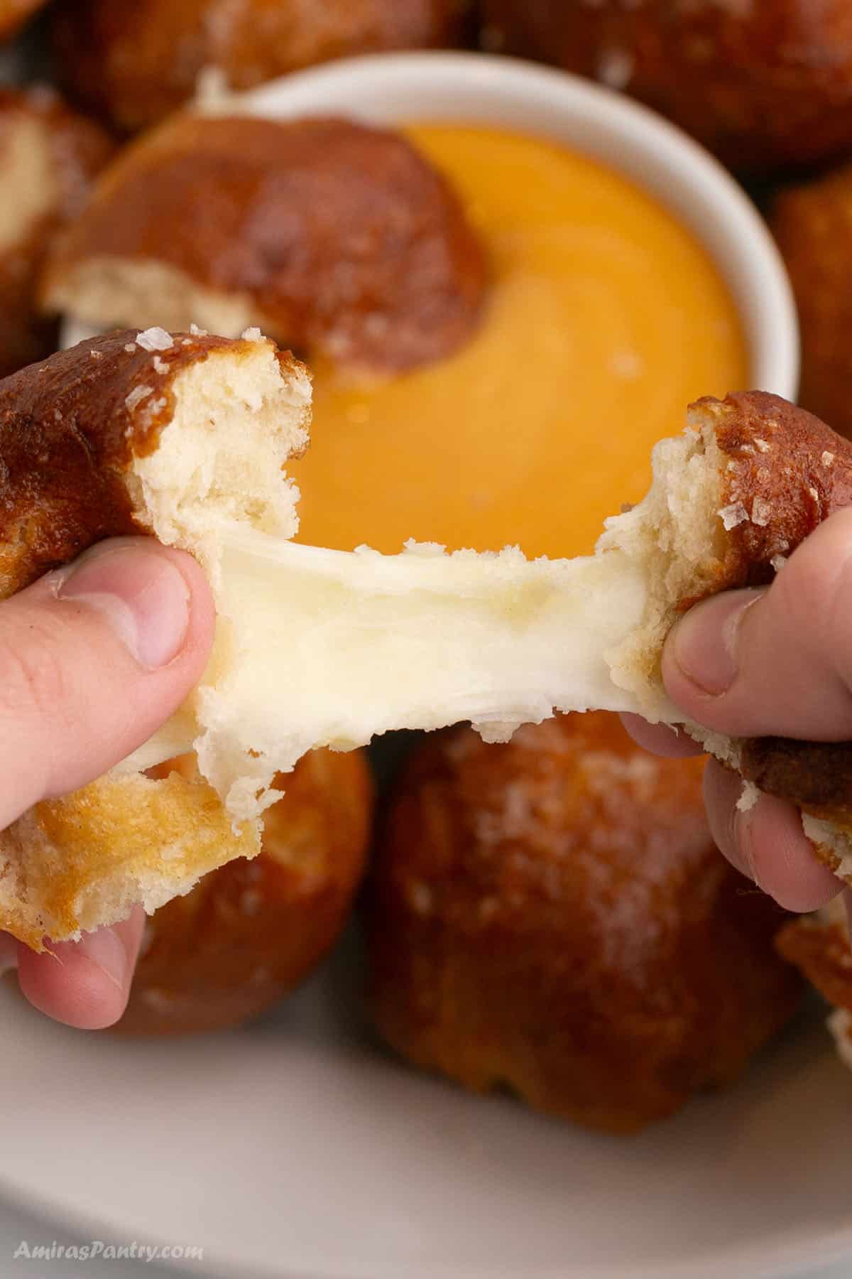  Hands pulling one pretzel apart showing melty cheese.