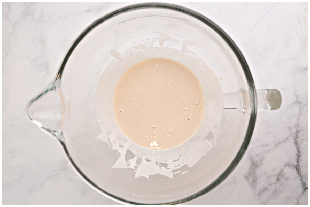 A glass bowl of a stand mixture with yeast and water.