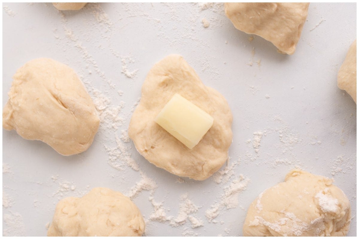 Dough balls on a surface with one stuffed with cheese.