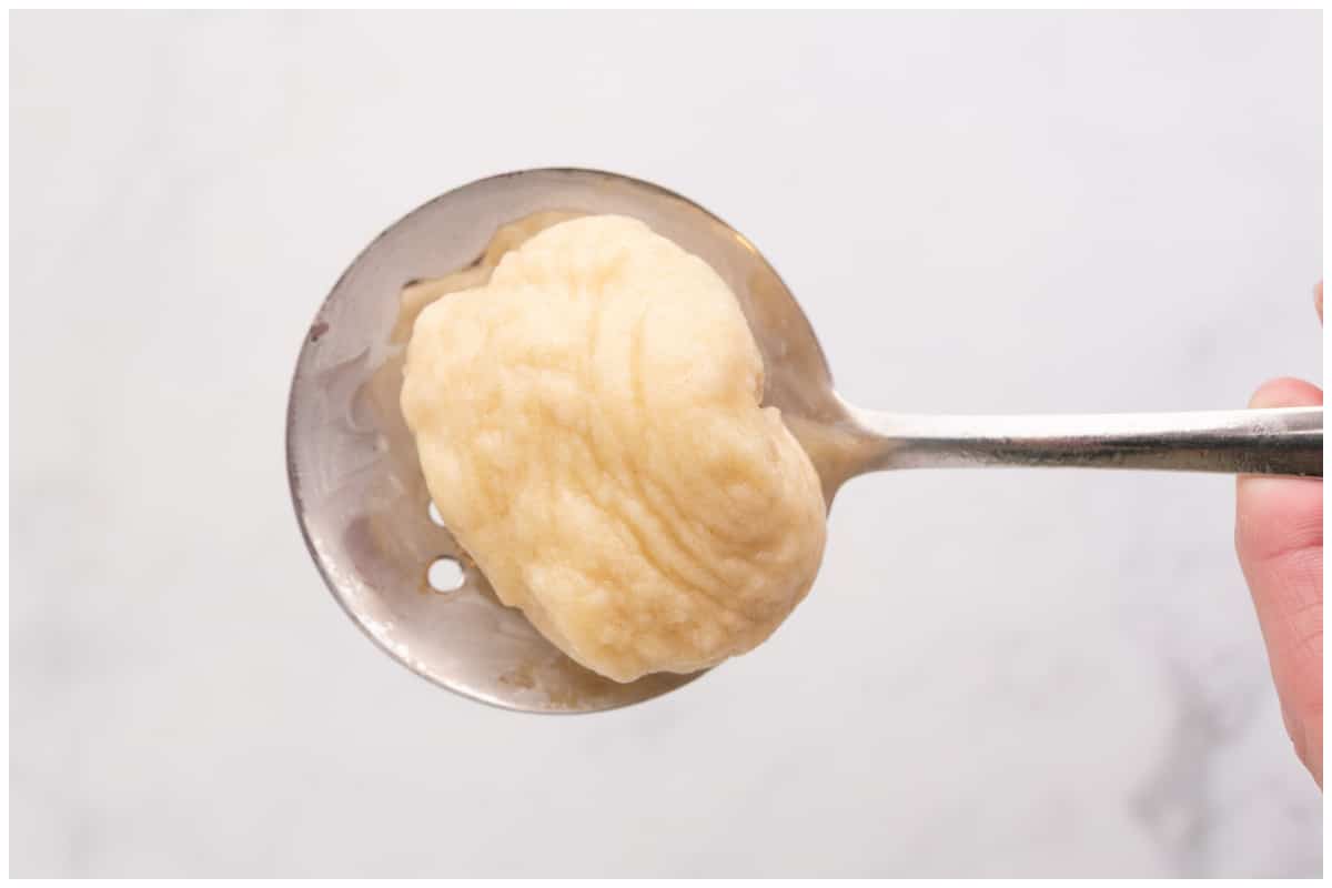 A hand holding a slotted spoon with one dough ball.