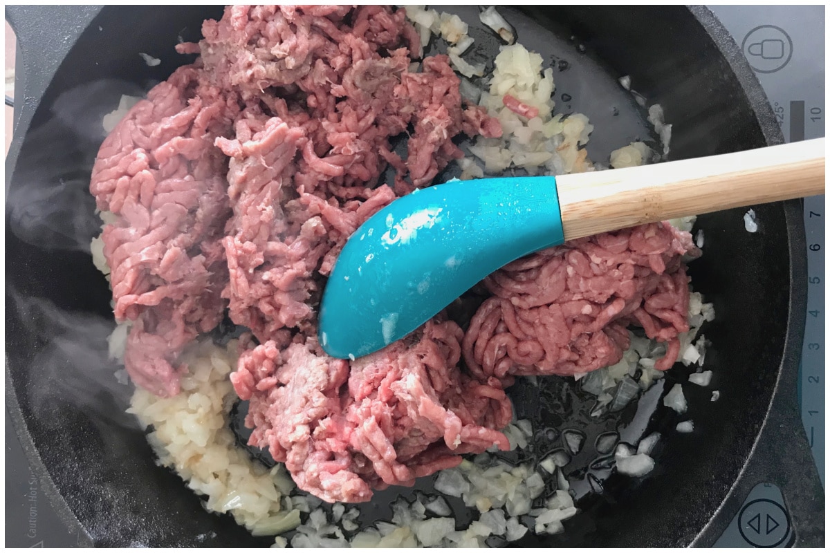 A cast iron skillet with ground beef and onion.