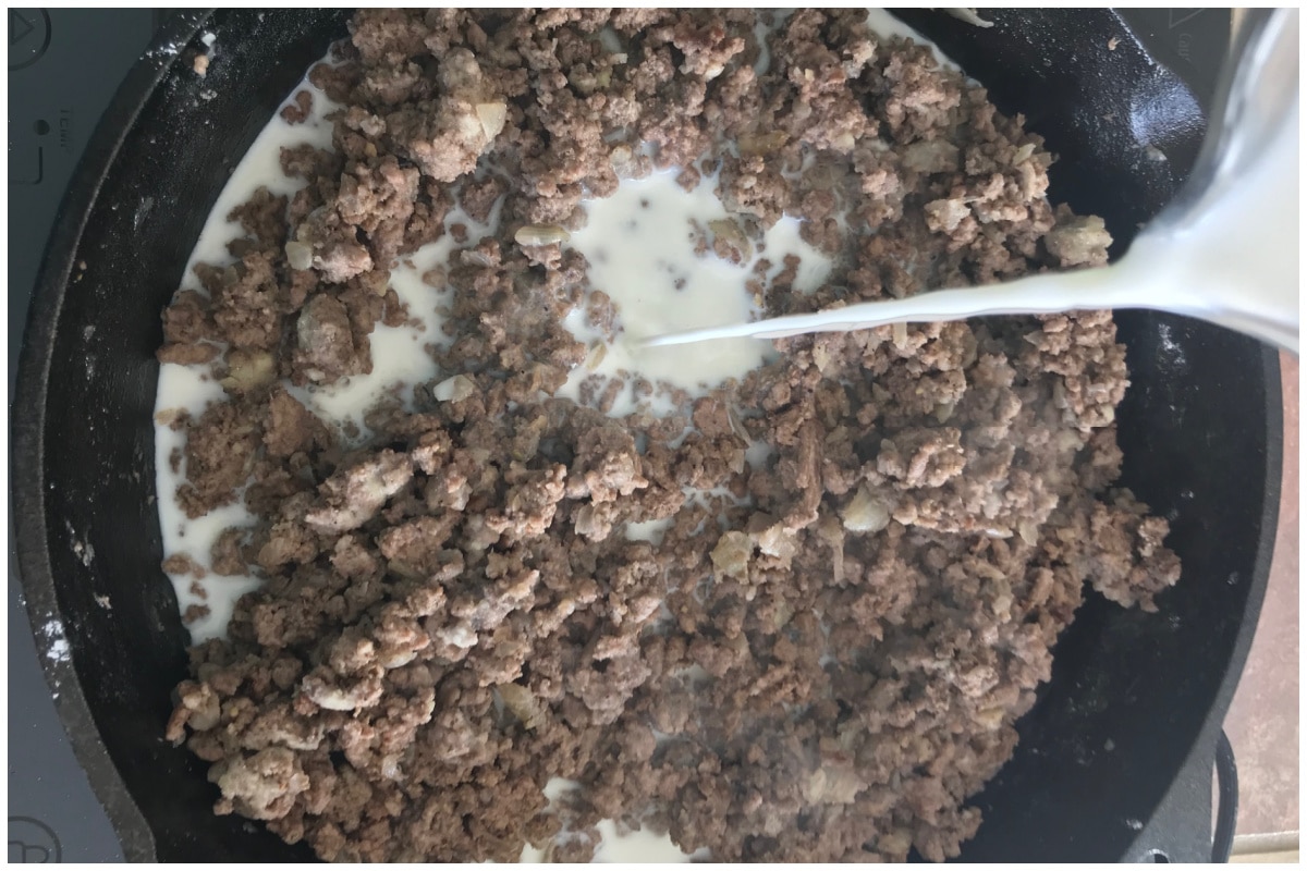 Pouring milk over a skillet of cooked ground beef.