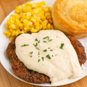 A dinner plate with cracker barrel fried steak, corn and a biscuit.