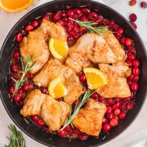 An overhead image of a skillet with orange cranberry chicken garnished with rosemary.