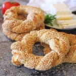 A pile of simit on a countertop with cheese in the back.