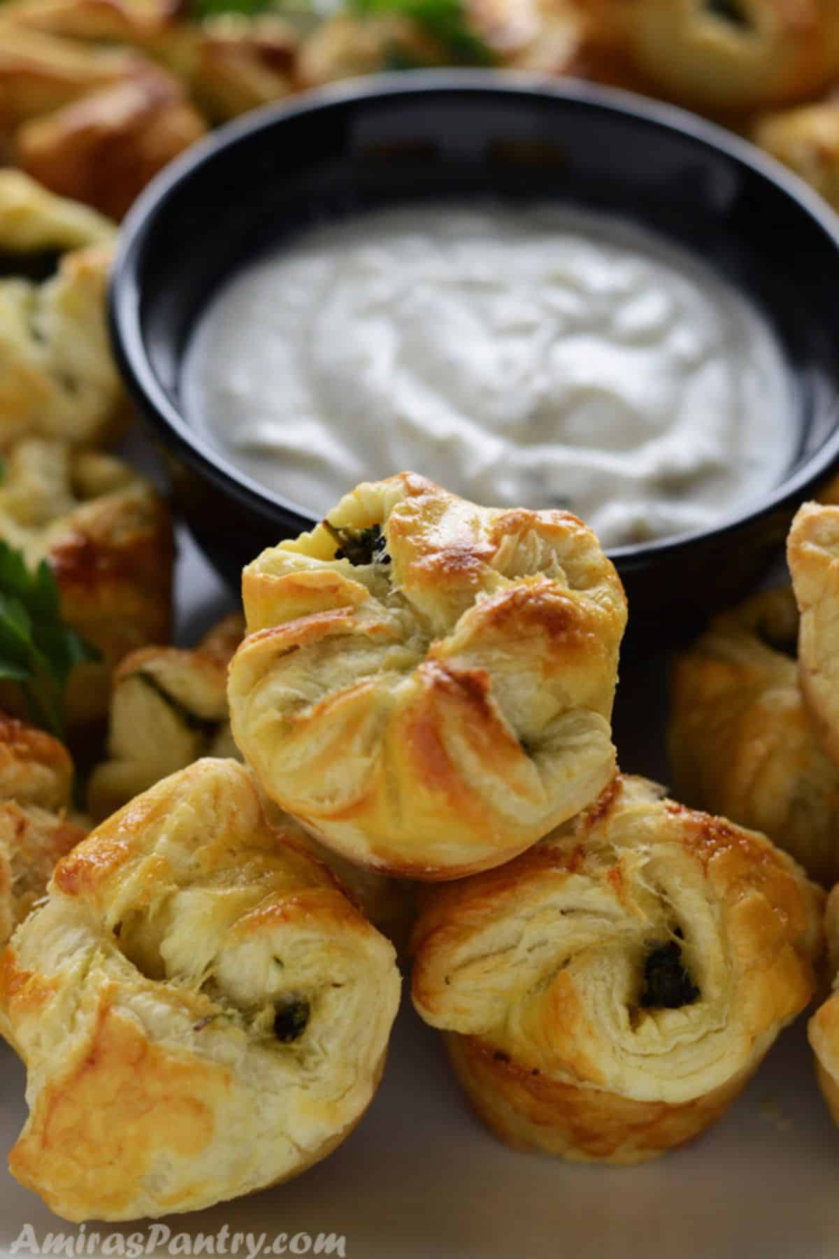 Spanakopita on a tray with a bowl of tzatziki dip in the back.